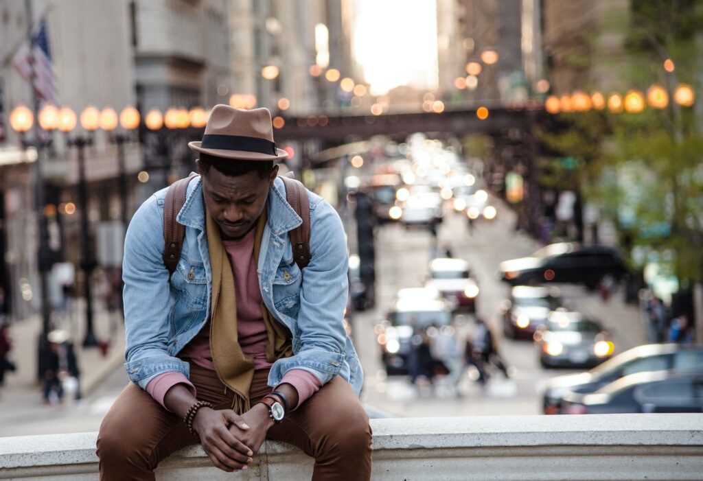 sad man sitting with his head down with street view in the background